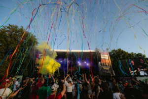 100 Kilo Herz Bunte Konfetti und Rauch in Gelb umgeben die Bühne beim Elbenwald Festival, während begeisterte Fans tanzen und feiern. Die lebendige Atmosphäre vereint Musik und Nerdkultur in einem unvergesslichen Erlebnis unter freiem Himmel.