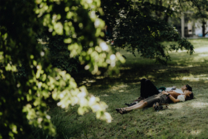 Zwei Personen liegen entspannt auf einer Wiese, umgeben von Bäumen, während sie das Elbenwald Festival genießen. Die Atmosphäre ist lebhaft und freundlich, ideal für Fans von Musik und Nerd-Kultur.