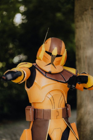 Ein kostümierter Teilnehmer in einer orangefarbenen Rüstung, inspiriert von Science-Fiction-Universen, posiert auf dem Elbenwald Festival. Die lebendige Atmosphäre kombiniert Musik und Nerd-Kultur, ideal für Fans von Cosplay und Gaming.