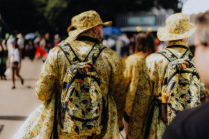 Zwei Besucher des Elbenwald Festivals tragen auffällige gelbe Regenjacken und Hüte mit Entenmotiven. Sie sind mit Rucksäcken ausgestattet und bewegen sich durch die Menge, umgeben von anderen Festivalteilnehmern.