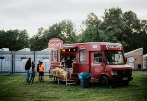 Ein roter Foodtruck von FritzCurry auf dem Elbenwald Festival, umgeben von Besuchern, die auf ihr Essen warten. Im Hintergrund sind Zelte und Bäume sichtbar, die zur Festivalatmosphäre beitragen. Ideal für hungrige Festivalteilnehmer.