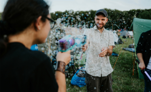 Zwei Festivalbesucher beim Elbenwald Festival spielen mit Wasserpistolen und erzeugen Seifenblasen auf einem grünen Festivalgelände. Im Hintergrund sind Zelte und andere Teilnehmer zu sehen, die die entspannte Atmosphäre genießen.