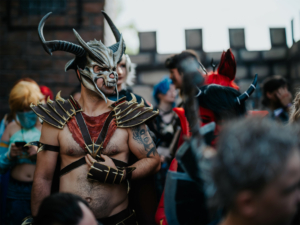 Ein männlicher Cosplayer mit einem eindrucksvollen Hornhelm und Rüstung steht im Mittelpunkt einer Menschenmenge auf dem Elbenwald Festival. Im Hintergrund sind weitere Teilnehmer in fantasievollen Kostümen zu sehen, die die aufregende Atmosphäre des Events widerspiegeln.