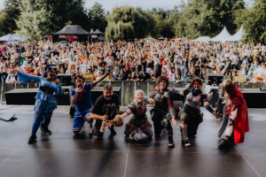 Elbenwald Cosplay Contest Bunt gekleidete Cosplayer posieren auf der Bühne des Elbenwald Festivals vor einer jubelnden Menge. Die Atmosphäre ist lebhaft und feierlich, mit Fans, die ihre Leidenschaft für Popkultur und Fantasy teilen.