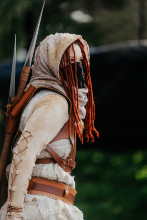 Elbenwald Cosplay Contest Kostümierte Person mit roten Dreadlocks und Maske, ausgestattet mit mehreren langen Klingen. Die Szene fängt die Atmosphäre des Elbenwald Festivals ein, wo Cosplay und Kreativität im Mittelpunkt stehen. Ideal für Fans von Fantasy und Nerd-Kultur.
