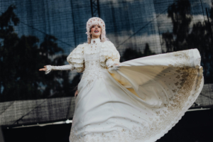 Elbenwald Cosplay Contest Eine Performer*in in einem eleganten weißen Kleid mit kunstvollen Details tanzt auf der Bühne beim Elbenwald Festival. Die Szenerie zeigt eine lebendige Atmosphäre, die den kreativen Geist des Festivals widerspiegelt.