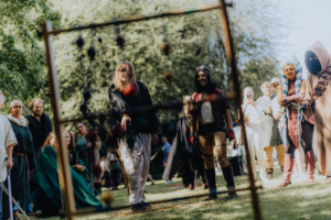 Die Roten Adler vs. 501st Teilnehmer des Elbenwald Festivals spielen ein Geschicklichkeitsspiel in fantasievoller Kleidung. Die Szene zeigt eine lebendige Atmosphäre mit verschiedenen Charakteren, die sich amüsieren und die kreative Gemeinschaft feiern.