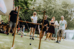 Die roten Adler Gruppe von Festivalbesuchern beim Elbenwald Festival, die an einem Spiel teilnehmen. Im Hintergrund sind Zelte und eine entspannte Atmosphäre im Grünen zu sehen. Die Teilnehmer tragen bunte Kleidung und genießen die Freizeitaktivitäten.