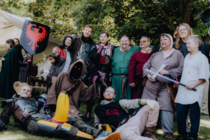 Die Roten Adler vs. 501st Gruppe von Cosplayern in verschiedenen Fantasiekostümen auf dem Elbenwald Festival, umgeben von Natur. Die Teilnehmer posieren fröhlich für die Kamera, während sie Requisiten und Accessoires aus der Nerdkultur halten.