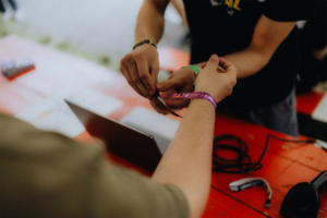 Hände einer Person, die ein Festivalarmband am Elbenwald Festival anlegt. Im Hintergrund ist ein Laptop und weiteres Festivalzubehör zu sehen. Die Szene vermittelt die Vorfreude und das Gemeinschaftsgefühl der Veranstaltung.