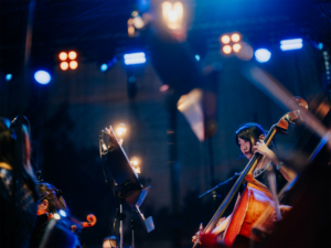 Elbenwald in Concert Musikerin spielt Cello auf der Bühne des Elbenwald Festivals, umgeben von bunten Lichtern und einer begeisterten Menge. Die Atmosphäre vereint Musik und Nerdkultur in einem einzigartigen Erlebnis für Fans.