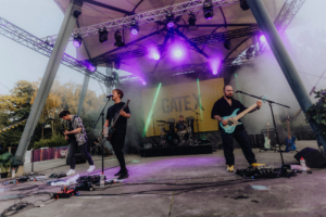 Gate X live Live-Auftritt der Band GateX auf dem Elbenwald Festival, mit bunten Lichtern und einer energiegeladenen Atmosphäre. Die Musiker spielen auf einer Bühne, umgeben von Nebel und einer begeisterten Menge. Ideal für Fans von Musik und Nerdkultur.