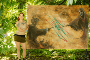 Frau steht neben einem großen Kunstwerk, das zwei Figuren in einem magischen Duell darstellt. Umgeben von grünen Bäumen, spiegelt die Szenerie die kreative Atmosphäre des Elbenwald Festivals wider, das Musik und Fantasie vereint.