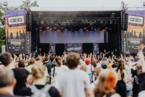 Kontrollverlust Bühne des Elbenwald Festivals mit begeistertem Publikum, das die Arme hebt. Im Hintergrund sind Banner mit dem Festival-Logo und den Auftritten zu sehen. Die Atmosphäre ist lebhaft und fröhlich, perfekt für Musik- und Nerdkultur-Fans.