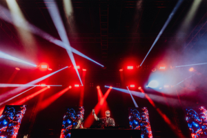 Bild: Rainer Keuenhof DJ auf der Bühne beim Elbenwald Festival, umgeben von bunten Lichtern und Nebel. Die energiegeladene Atmosphäre schafft eine Verbindung zwischen Musik und Nerd-Kultur, während das Publikum begeistert mitfeiert.