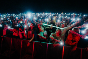 Nerds at Raves live Festivalbesucher beim Elbenwald Festival, die mit leuchtenden Handys und Lichtstäben die Stimmung anheizen. Die Menge ist in Feierlaune und zeigt ihre Begeisterung für die Musik und das Gemeinschaftserlebnis unter dem nächtlichen Himmel.