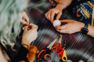 Retro-Basteln Zwei Personen arbeiten an Bastelprojekten während des Elbenwald Festivals. Auf dem Tisch liegen verschiedene Scheren, eine weiße Kugel und Bastelmaterialien. Die kreative Atmosphäre fördert den Austausch von Ideen und handwerklichen Fähigkeiten.