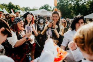 Bunt gekleidete Festivalbesucher beim Elbenwald Festival, umgeben von Cosplay-Kostümen, die verschiedene Charaktere darstellen. Fröhliche Gesichter und kreative Outfits schaffen eine lebendige Atmosphäre voller Begeisterung und Gemeinschaft.