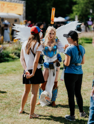 Cosplayer mit Engelsflügeln und aufwändiger Kostümierung beim Elbenwald Festival, umgeben von interessierten Besuchern. Die Szene zeigt die kreative Atmosphäre des Festivals, das Musik und Nerdkultur vereint.