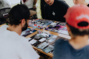 Spieler beim Elbenwald Festival, die an einem Tisch ein Kartenspiel spielen. Auf dem Tisch sind Karten, Würfel und Spielmaterialien verteilt, während die Teilnehmer konzentriert strategische Entscheidungen treffen und sich austauschen.