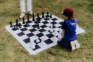 Ein Kind spielt auf einem großen Schachbrett aus Kunststoff mit weißen und schwarzen Figuren beim Elbenwald Festival. Die Szene zeigt die Kombination von Spiel und Interaktion in einer entspannten Festivalatmosphäre.