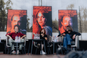 Stranger Things Synchro-Talk mit Peter Flechtner, Franciska Friede und Martin Sabel Paneldiskussion auf dem Elbenwald Festival mit Sprechern vor "Stranger Things"-Plakaten. Die Teilnehmer sitzen auf Stühlen, umgeben von Wasserflaschen, während sie über die Serie diskutieren. Einblicke in die Nerd-Kultur und die Faszination für die Show.