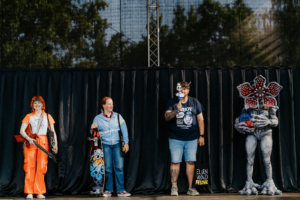Stranger Things Cosplay Contest Vier Teilnehmer in kreativen Kostümen stehen auf der Bühne beim Elbenwald Festival. Von einer Musikerin mit Gitarre bis zu einem beeindruckenden Kostüm mit floralen Elementen, die Vielfalt und den Spaß des Festivals widerspiegelnd.