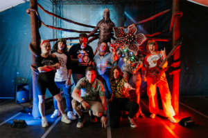 Stranger Things Cosplay Contest: Gruppenselfie von Festivalbesuchern in kreativen Kostümen vor einem beeindruckenden Bühnenhintergrund. Die Teilnehmer posieren mit Requisiten und einer fantasievollen Figur, die von der Popkultur inspiriert ist, und zeigen die lebendige Atmosphäre des Elbenwald Festivals. Foto: Robin Schmiedebach
