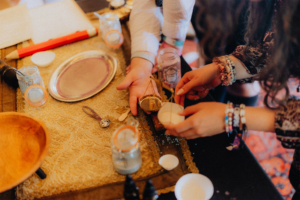 Zwei Personen arbeiten gemeinsam an einem Tisch, der mit verschiedenen Gegenständen wie einem silbernen Tablett, Gläsern und einer Taschenuhr dekoriert ist. Die kreative Atmosphäre spiegelt die handwerklichen Aktivitäten des Elbenwald Festivals wider.