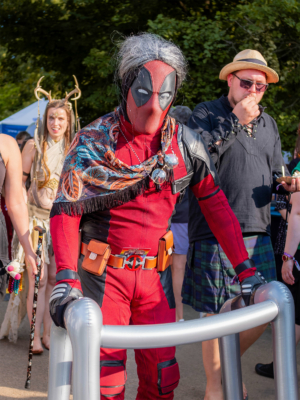 Ein Teilnehmer des Elbenwald Festivals in einem detaillierten Deadpool-Kostüm, umgeben von weiteren Festivalbesuchern in verschiedenen Kostümen. Die Szene zeigt die lebendige Atmosphäre und die kreative Kostümgestaltung der Veranstaltung.