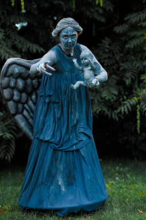 Eine gruselige Kostümfigur mit Flügeln und einem Kind in der Hand, die auf dem Elbenwald Festival steht. Die Figur ist komplett in Blau gekleidet und hat ein bedrohliches Gesicht, was die kreative und fantasievolle Atmosphäre des Festivals widerspiegelt.