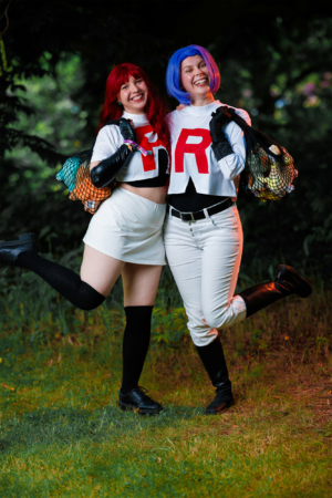 Zwei Cosplayerinnen in bunten Kostümen bei dem Elbenwald Festival, lächelnd und posierend. Die eine trägt ein rotes und die andere ein blaues Haar, beide zeigen mit ihren Outfits eine kreative Interpretation von Charakteren aus der Popkultur.