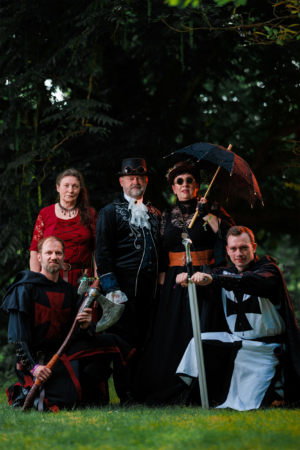 Gruppe von vier kostümierten Personen auf dem Elbenwald Festival, gekleidet in fantasievolle Outfits mit Steampunk-Elementen und mittelalterlichen Akzenten. Die Szene zeigt eine kreative Mischung aus Musik und Nerd-Kultur im Freien.