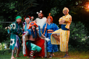 Sechs verkleidete Teilnehmer des Elbenwald Festivals posieren in einem grünen Wald. Die Gruppe zeigt eine bunte Mischung aus Fantasie- und Comiccharakteren, darunter ein Pirat und verschiedene traditionelle Kostüme, die die kreative Atmosphäre des Festivals widerspiegeln.