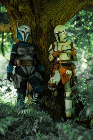 Zwei Cosplayer in detailreichen Mandalorian-Rüstungen stehen an einem Baum im Grünen. Die Szenen zeigen die kreative Atmosphäre des Elbenwald Festivals, wo Musik und Nerd-Kultur aufeinandertreffen.