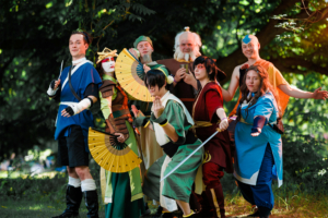 Gruppe von Cosplayern in bunten Kostümen, inspiriert von einer beliebten Animationsserie, posiert fröhlich im Freien. Die Teilnehmer zeigen kreative Details ihrer Outfits und Accessoires, während sie die Atmosphäre des Elbenwald Festivals genießen.