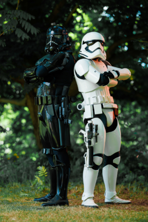 Zwei Cosplayer in beeindruckenden Star Wars-Outfits, ein schwarzer Stormtrooper und ein klassischer Stormtrooper, stehen Rücken an Rücken auf einer Wiese beim Elbenwald Festival, umgeben von grüner Natur und festlicher Atmosphäre.