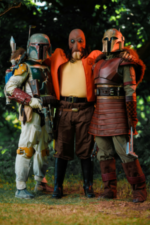 Drei Cosplayer in detailreichen Kostümen aus dem Star Wars-Universum, darunter Boba Fett, pose im Freien beim Elbenwald Festival. Die Veranstaltung kombiniert Musik und Nerd-Kultur und zieht Fans aus verschiedenen Bereichen an.