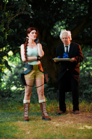 Cosplay von Lara Croft und einem Butler beim Elbenwald Festival. Die Szene zeigt den Kontrast zwischen dem abenteuerlustigen Charakter und dem eleganten, formellen Outfit des Butlers, umgeben von grüner Natur.