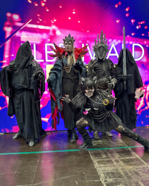 Gruppe von Cosplayern in beeindruckenden, fantasievollen Kostümen auf dem Elbenwald Festival, umgeben von einer bunten, beleuchteten Kulisse. Die Charaktere zeigen eine Mischung aus dunkler Magie und mystischen Elementen, die die Festivalatmosphäre unterstreichen.