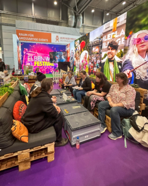 Besucherinnen und Besucher des Elbenwald Festivals sitzen in einem gemütlichen Bereich mit Palettenmöbeln, umgeben von bunten Wandgestaltungen, die die Atmosphäre eines kreativen und lebhaften Events widerspiegeln.