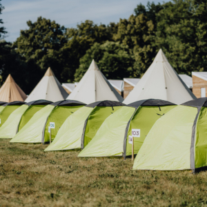 Zeltplatz auf dem Elbenwald Festival mit leuchtend grünen Zelten und nummerierten Stellplätzen, umgeben von Bäumen und einer entspannenden Atmosphäre, ideal für Festivalbesucher und Nerd-Kultur-Fans.